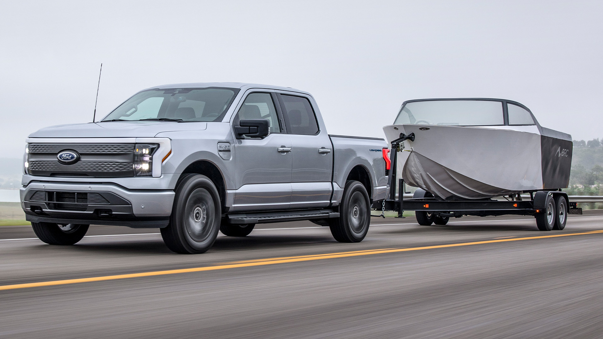 f-150-lightning-hero-1-1 A Ford F-150 Lightning tows a boat down the highway.